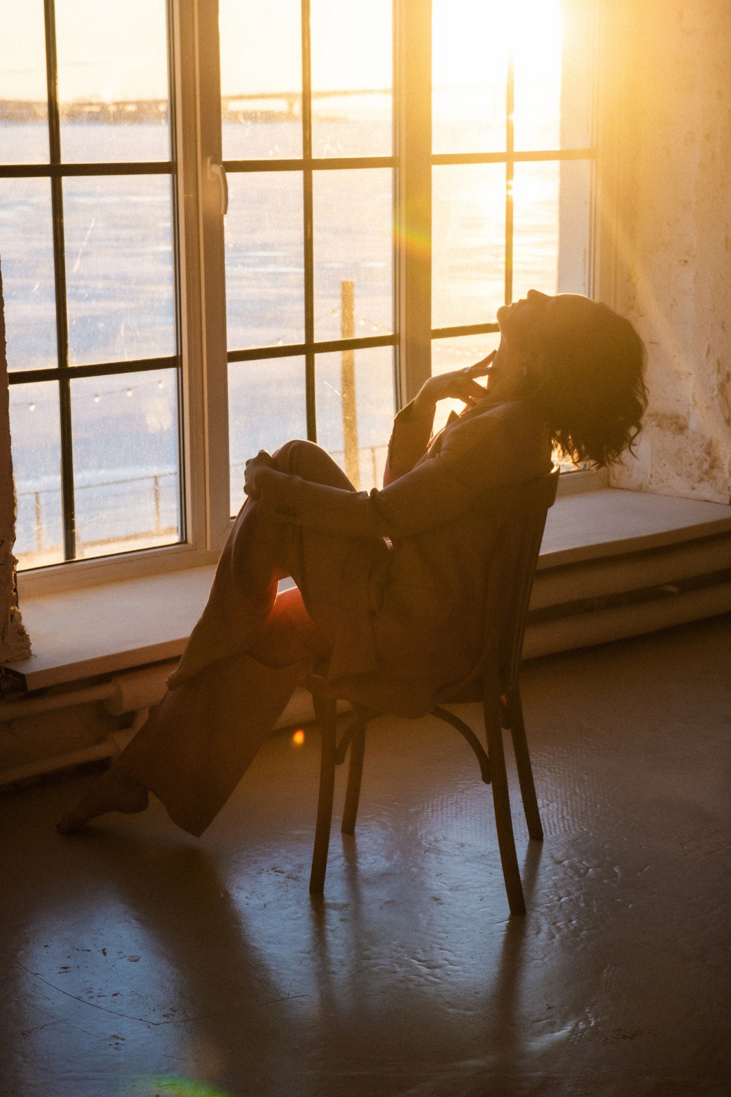 Middle-aged woman basking in soft morning sunlight by the window, soaking up Vitamin D and reflecting peace and warmth.
