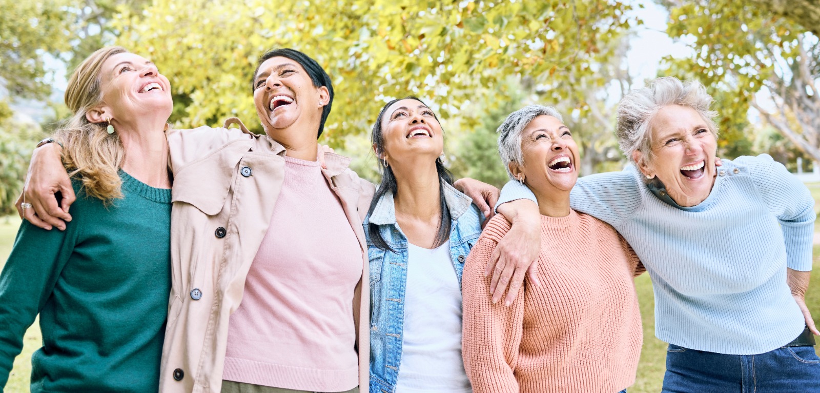 Group of joyful midlife women laughing together in a park, symbolizing emotional wellness and hormonal balance during menopause.