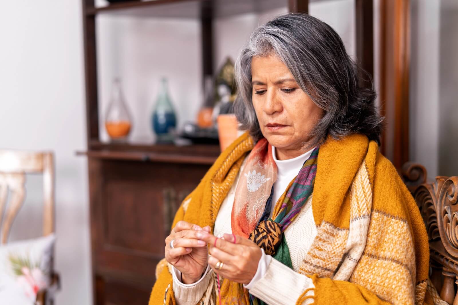 Midlife woman sitting pensively, wrapped in a shawl, appearing thoughtful and distracted — symbolizing brain fog and mental health struggles in menopause.