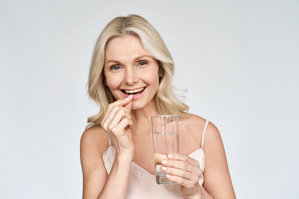 Smiling midlife woman taking a supplement with water, symbolizing Glutathione support during menopause.