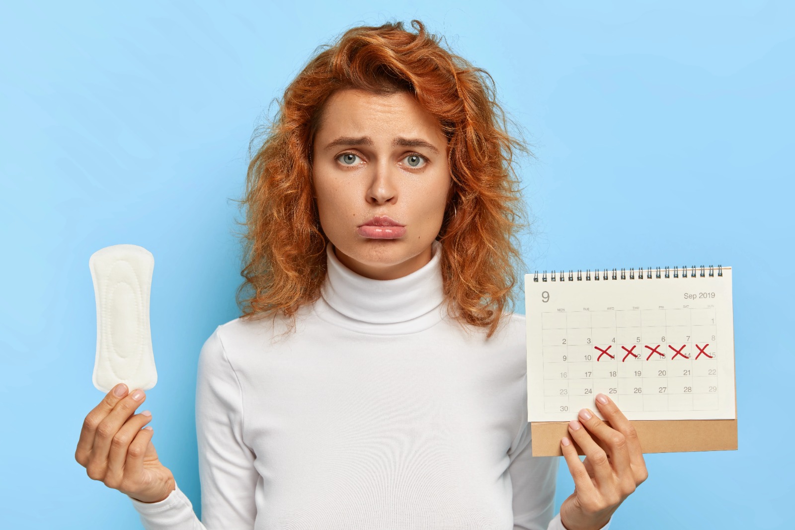 Young woman looking confused while holding a calendar and sanitary pad — concept of irregular periods or missed cycles.