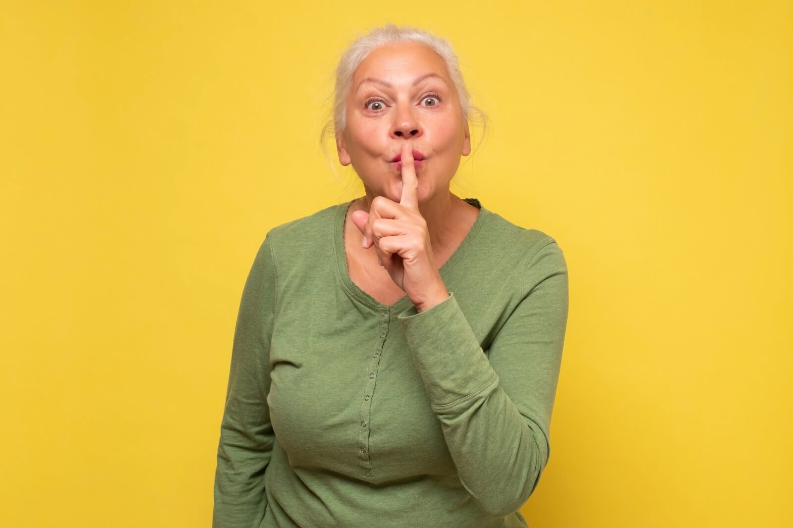 Playful older woman making a 'shh' gesture, hinting at secrets with a smile.