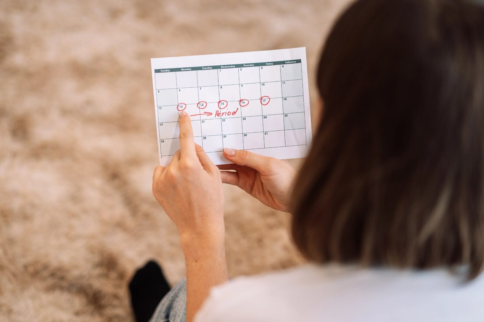 A woman holding a calendar and pointing to marked period dates with red circles.
