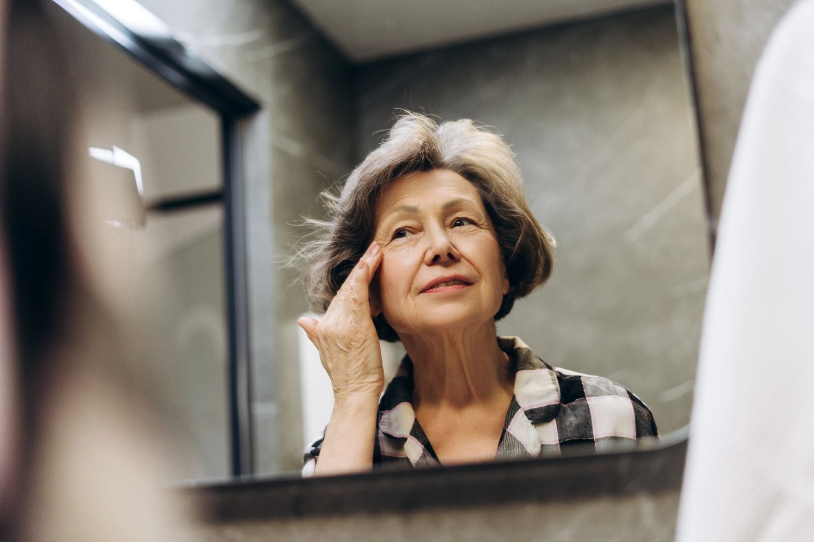 Mature woman looking in the mirror, reflecting on menopause and mental health problems with self-awareness.