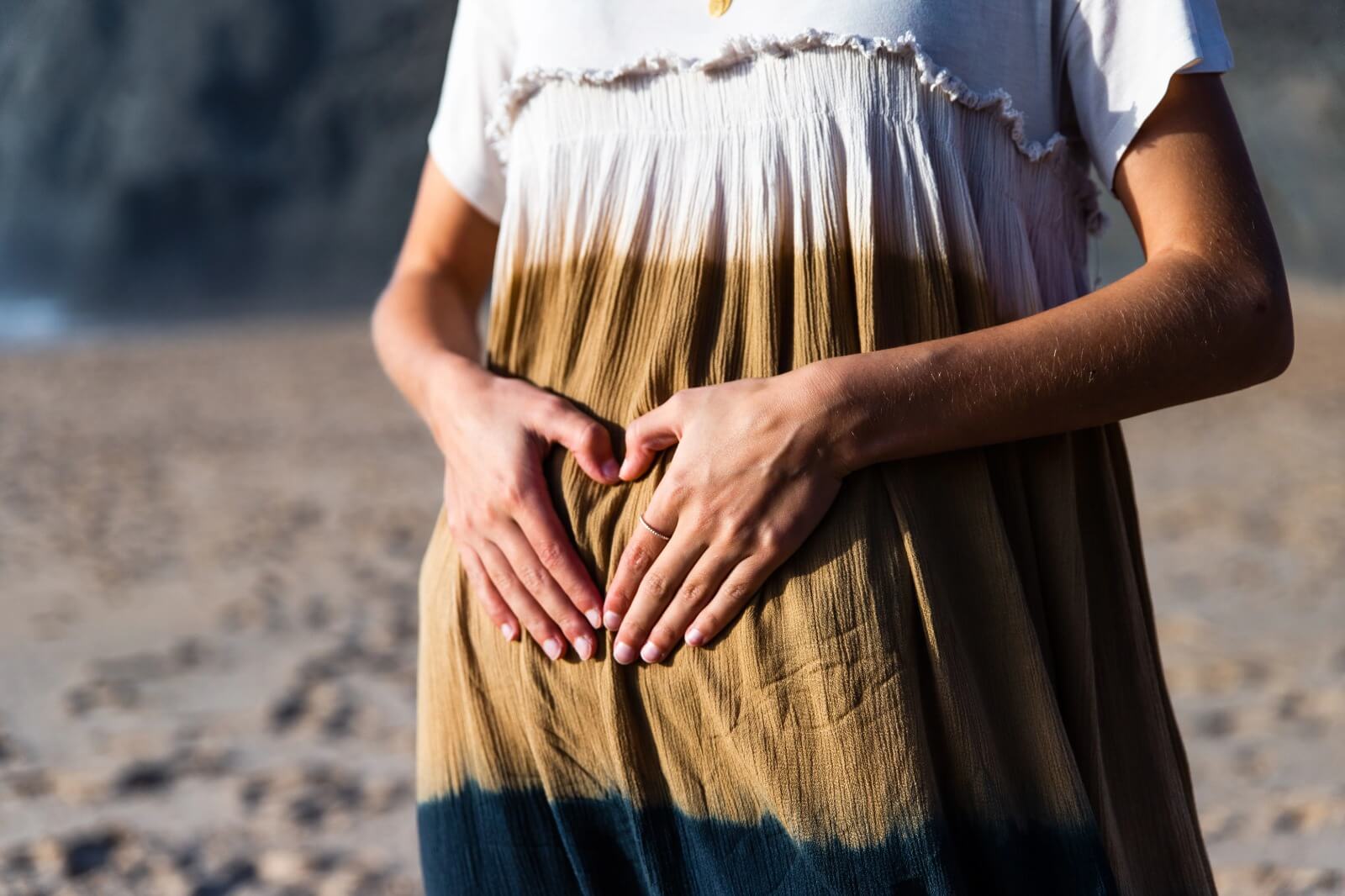 Pregnant woman forming heart shape on belly at beach