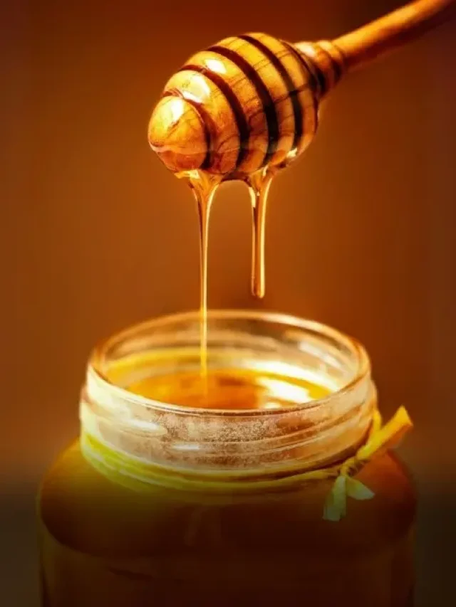 A spoon of honey dripping into a jar of honey